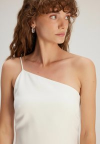 Top en satin blanc avec un design asymétrique et une bretelle. Texture lisse et coupe ajustée, mettant en valeur le décolleté.
