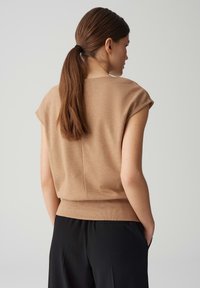 Beige gebreide top met kapmouwen, textuurafwerking en een aansluitende onderboord. Draag met zwarte broek, met een achteraanzicht.