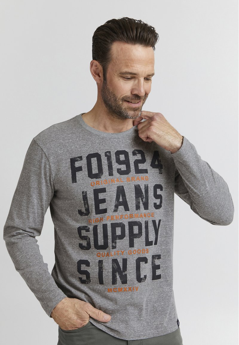 Grå langærmet T-shirt lavet af blødt stof, med fed sort og orange skærmtrykt tekst. Enkel rund hals og afslappet pasform.