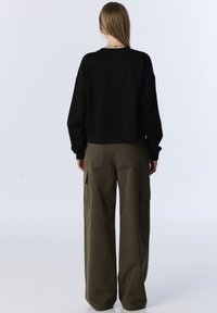 Zwarte cropped sweatshirt met lange mouwen, gecombineerd met olijfgroene cargobroek met zijzakken en een rechte pasvorm.