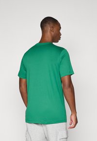 Camiseta verde de manga corta hecha de tejido suave, con cuello redondo clásico y corte regular, mostrada desde la parte de atrás.