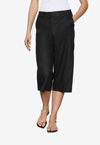 Pantalones culotte de lino negro con una cintura ajustada, bolsillos frontales y un diseño corto, combinados con sandalias de tiras metálicas.