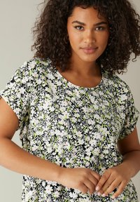 Blomsterbluse med rund halsudskæring, korte ærmer og en sort baggrund med hvide og lyserøde blomster. Let og blød stof med et levende design.