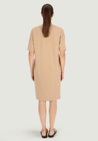 Beżowa sukienka krótki rękaw, luźny krój, do kolan, wykonana z gładkiego materiału bawełnianego, z okrągłym dekoltem i minimalnymi detalami przeszycia.