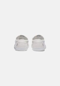 White canvas sneakers with a low-top design, rubber soles, and a logo on the back. Features minimal stitching and clean lines.