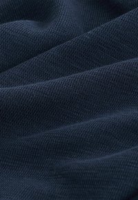 Tissu bleu marine foncé avec un motif texturé et tissé serré, présenté en gros plan avec des plis doux et des ombres.