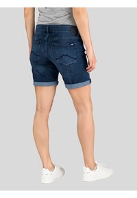 Jeansshorts met omgeslagen zoom, donkere wassing, vijf-pocket ontwerp en gestikte accenten op de achterzakken. Gepaard met witte sneakers.