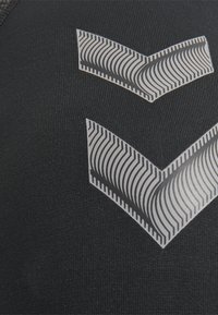 Sort atletisk stof med to grå og hvide chevron-mønstre med bølgende linjer, synlig stiktektur i baggrunden.