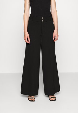Czarne spodnie o szerokich nogawkach z dwoma metalowymi guzikami w pasie, wykonane z gładkiego materiału, o wysokim stanie i dopasowanym kroju.