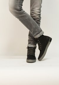 Botas de ante negras hasta el tobillo con suelas de goma gris, que cuentan con ojales de metal, cordones grises y jeans de mezclilla gris arremangados.