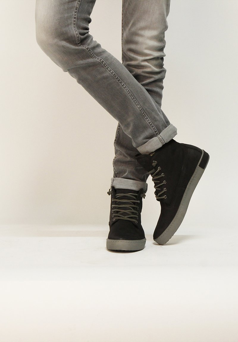 Botas de ante negras hasta el tobillo con suelas de goma gris, que cuentan con ojales de metal, cordones grises y jeans de mezclilla gris arremangados.