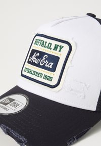 Gorra azul marino y blanca con un visor deshilachado, que presenta un parche bordado que dice "Buffalo, NY New Era Established 1920." Ajuste personalizado.