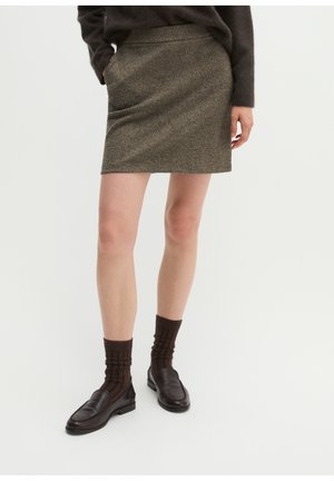 Femme portant une mini-jupe en tweed marron, des chaussettes texturées marron foncé et des mocassins en cuir marron foncé sur un fond uni.