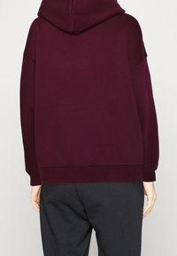 Sudadera burdeos con capucha, corte amplio, puños y dobladillo acanalados, con textura suave y diseño simple de color sólido.