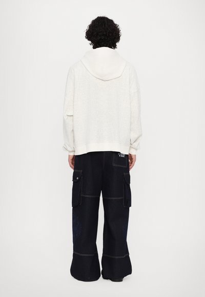 Hoodie blanc avec motif texturé et cordon de serrage, associé à un pantalon cargo noir à jambes larges avec poches latérales et couture contrastante.