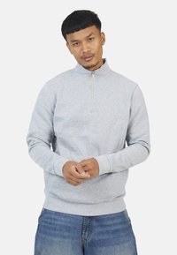 Lichtgrijze sweatshirt met ritssluiting en lange mouwen, geribbelde manchetten en een zachte textuur, gecombineerd met blauwe denim jeans.
