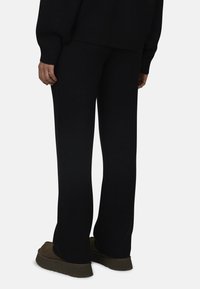 Czarny komplet dresowy z dzianiny, składający się z szerokich spodni i prążkowanego swetra. Materiał ma miękką fakturę i luźny krój, idealny do komfortowego noszenia.