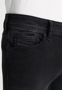 Svarta denimjeans har en figurnära design med framträdande sömmar, en frampocket och en diskret logotyp på insidan av fickan.