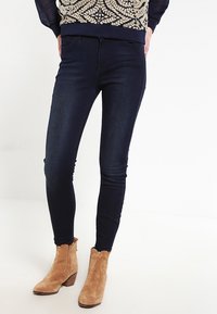 Mörkblå skinny jeans med en jämn textur, kombinerade med beige mocka ankellånga stövlar med klack och dragkedjedetalj.