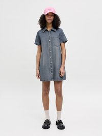 Denim skjortekjole med korte ermer, frontlukking med knapper, enkelt brystlomme, og en avslappet passform. Båret sammen med en rosa caps og svarte loafers.