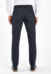 Pantalones azul marino oscuros fabricados con un tejido suave, que presentan un corte entallado, dos bolsillos traseros con botones y detalles de pliegues a lo largo de las piernas.