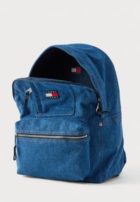 Modrý rifle batoh s veľkou hlavnú priehradkou, predným vreckom na zips a nášivkou s logom. Má zaoblený vrch a pevné šitie.