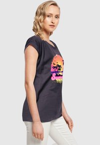 Mørk grå T-shirt med korte, oprullede ærmer, der har et farverigt solnedgangsgrafik med palmer og teksten "Summer Vibes" i livlige farver.