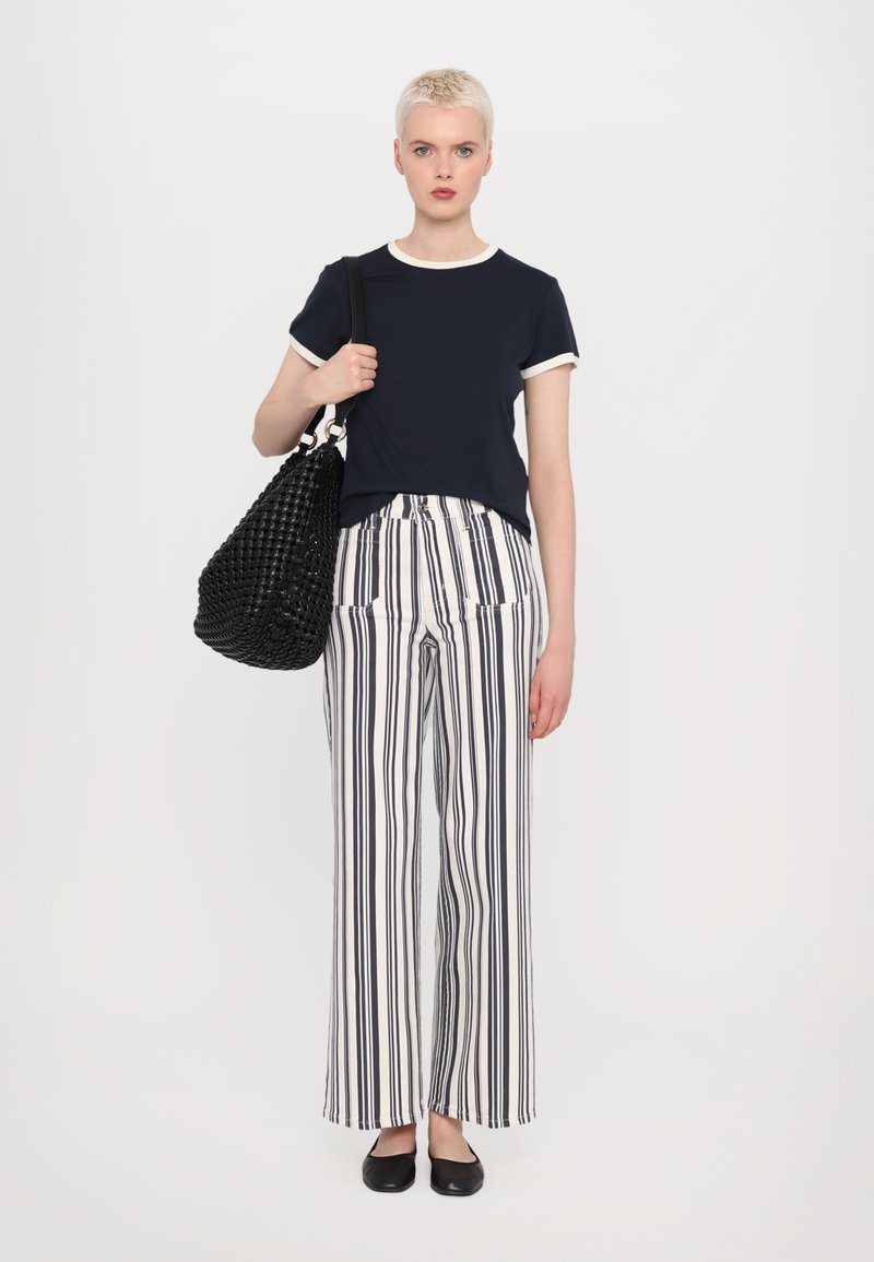 T-shirt marine avec des bordures blanches, un pantalon large à rayures verticales noir et blanc, et un sac à main noir texturé, associé à des ballerines noires.