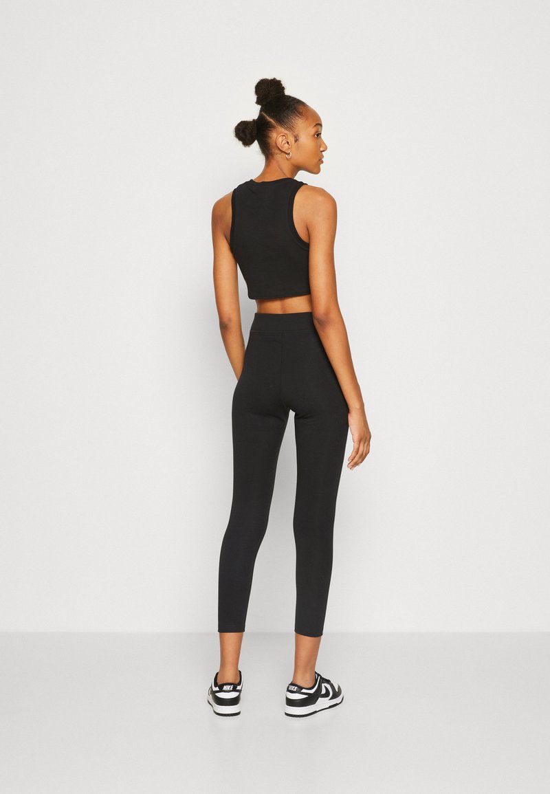 Crop top de sport noir et leggings taille haute, design ajusté, texture lisse, associé à des chaussures de sport noir et blanc.