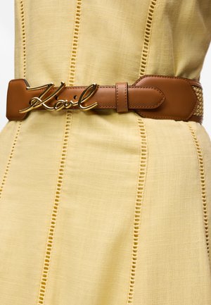 Φόρεμα ανοιχτού κίτρινου χρώματος με κατακόρυφες ραμμένες δαντέλες, συνδυασμένο με καφέ δερμάτινη ζώνη που διαθέτει χρυσή αγκράφα με τη λέξη "Karl".