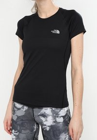Svart kortärmad sport-t-shirt med rund halsringning och en liten logotyp på bröstet, kombinerad med mönstrade svarta och gråa leggings.