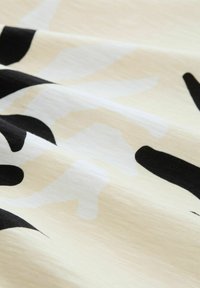 Close-up van lichte stof met zwarte en beige abstracte vormen en een gestructureerd geweven patroon.