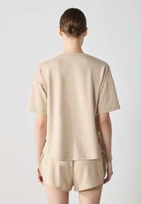 Beige bomullströja med korta ärmar och avslappnad passform, ihop med matchande shorts. Slät textur och enkel design.
