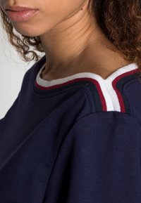 Námořnický bavlněný top s kulatým výstřihem a bílými, červenými a námořnickými pruhy. Tkanina má hladkou texturu, která zdůrazňuje uvolněn�ý design.