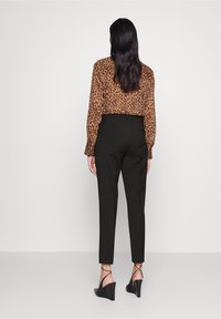 Hnědá halenka s leopardím vzorem a dlouhými rukávy, zastrčená do černých upravených kalhot. Černé klínové podpatky dotvářejí outfit.