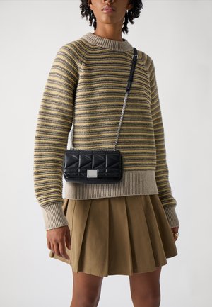 Schwarze gesteppte Handtasche mit einem silbernen Kettenriemen, im Crossbody-Stil getragen. Sie hat eine rechteckige Form und eine metallische Akzentuierung auf der Vorderseite.