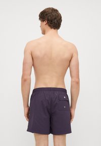 Fioletowe szorty kąpielowe z elastycznym pasem i tylną kieszenią. Wykonane z lekkiego materiału, charakteryzujące się gładką teksturą i minimalistycznym wzornictwem.