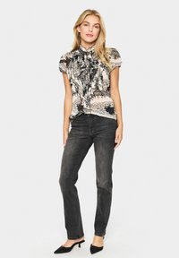 Ziedu raksta blūze mīkstā audumā ar viļņotu apkakli un īsām piedurknēm, kopā ar tumšām pieguļošām džinsām un melniem šauriem apaviem.