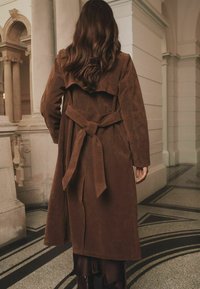 Cămașă de trench din suede maro, cu guler lat, talie cu curea și mâneci lungi. Prezintă o textură netedă și moale și are o lungime până la genunchi.