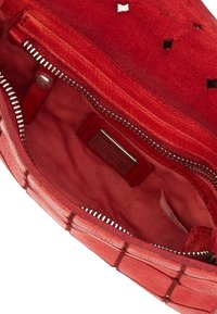 Interno di una borsa in pelle scamosciata rossa con una texture liscia, dotato di una tasca con zip, foderato di rosa e con un'etichetta metallica. Il design include piccoli dettagli ritagliati.