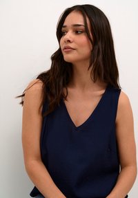 Top fără mâneci de culoare bleumarin cu un decolteu adânc în V, realizat dintr-un material neted; caracteristici de cusături minime și o strălucire subtilă.
