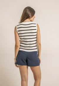 Haut en maille sans manches rayé en blanc et noir avec des bords festonnés, associé à un short bleu marine. La maille présente des rayures verticales et une texture côtelée.