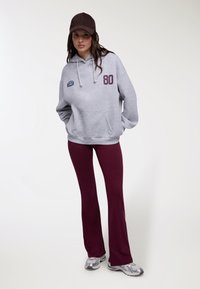 Felpa grigia con cappuccio e tasca frontale, con la scritta "80" color vinaccia. Abbinata a pantaloni a zampa color vinaccia e scarpe sportive argento.