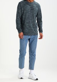 Mörk teal skjorta med långa ärmar och struktur, ljusblå tapered jeans och vita träningsskor med svarta detaljer. Enkel, avslappnad outfit.