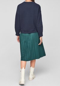 Marinblå sweatshirt med nedhasade axlar, i kombination med en plisserad grönblå kjol. Kjolen når knäna och har en mjuk textur. Vita ankelstövlar fulländar looken.