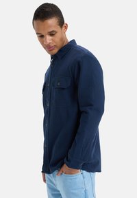 Marineblauwe, lange mouwen shirt met twee borstzakken en bruine knoopaccenten; gemaakt van een textiel met structuur; ontspannen pasvorm.