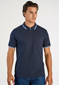 Marinblå polo t-shirt med dragkedja i kragen, med ljusblå randiga detaljer på kragen och ärmarna. Slät textur, figurnära design.