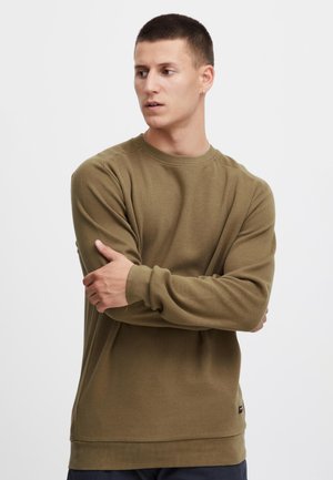 Oliven grønn langermet genser laget av teksturert stoff, med rund hals, ribbede mansjetter og rett kant. Diskret logo-detall nær kanten.