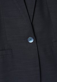 Blazer marine en tissu texturé, doté d'un seul bouton rond en nacre, de deux poches latérales et de revers crantés.