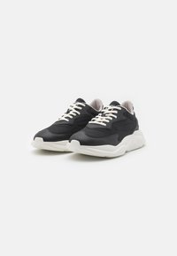 Scarpe sportive nere con tomaia in tessuto testurizzato, lacci bianchi e suola bianca spessa; presenta un design affusolato con un logo discreto.